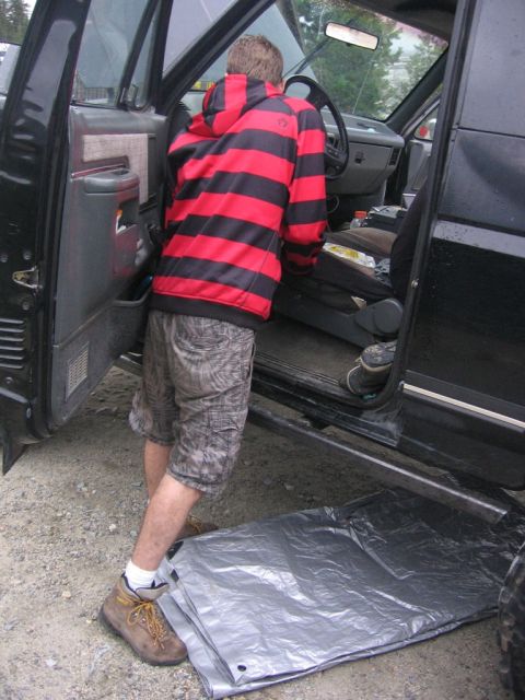 1989 Ford Bronco - A person enters a black truck, with a tarp laid out on the ground beside the door.