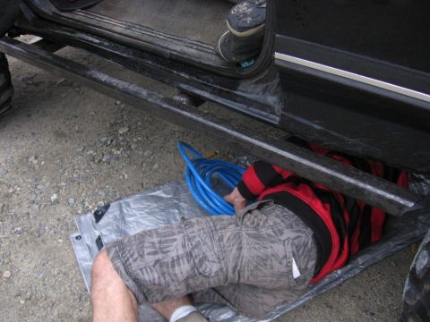 1989 Ford Bronco - Person works on vehicle undercarriage, using a blue hose and lying on a tarp.