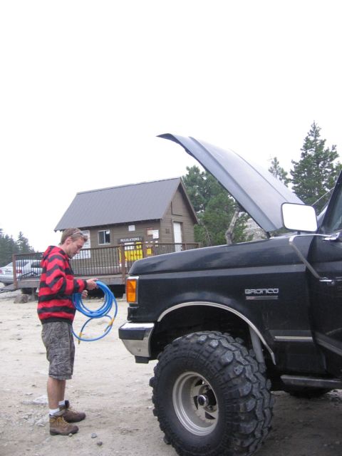 1989 Ford Bronco - A person stands next to a black Ford Bronco with its hood open, holding a blue hose.