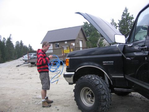 1989 Ford Bronco - A person stands next to a black 1989 Ford Bronco with the hood open, holding a blue hose.