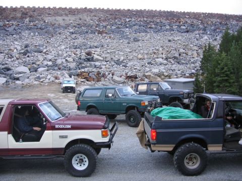 1989 Ford Bronco - Several SUVs are parked on a gravel lot with a rocky embankment in the background.