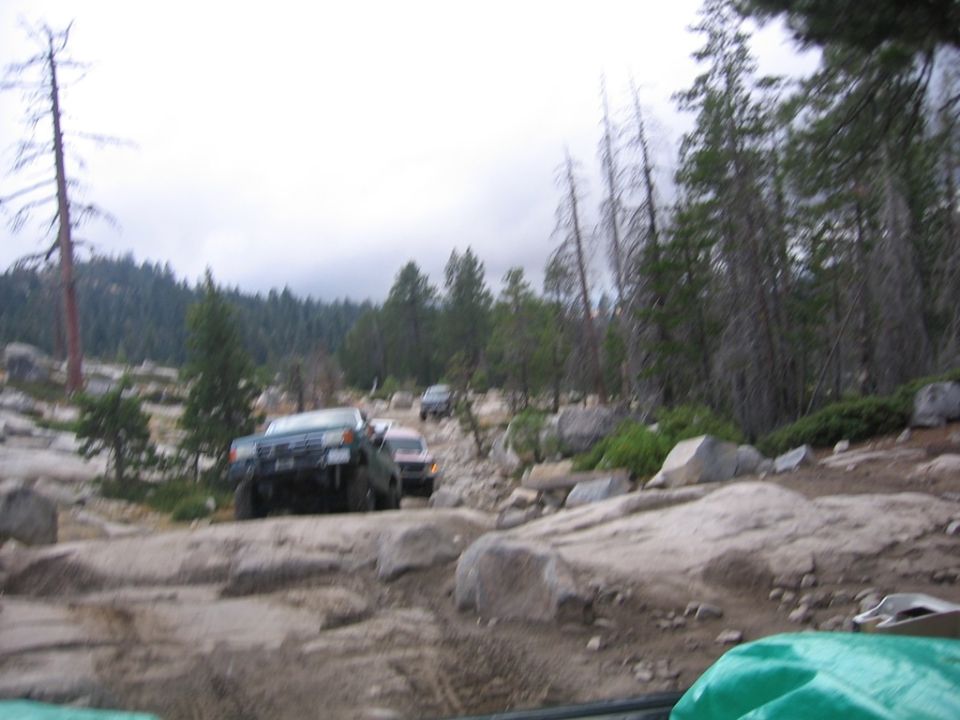 Several off-road vehicles navigate a boulder-strewn path through a forest
