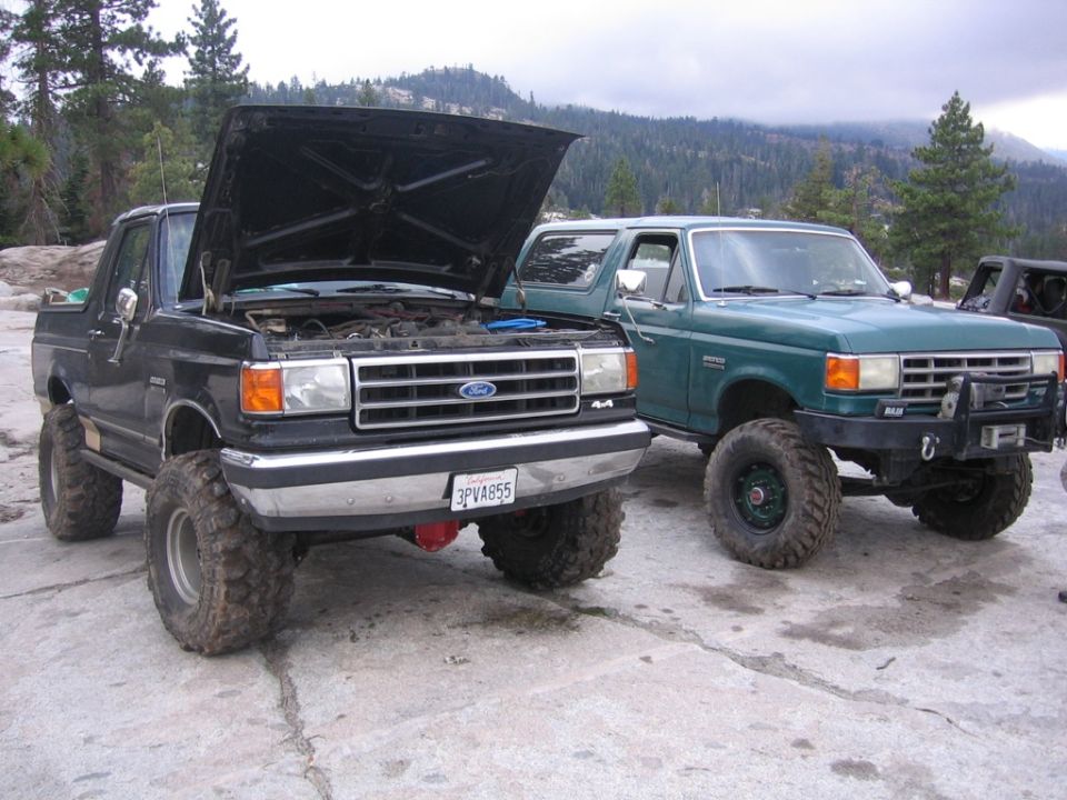 Two lifted Ford Broncos parked on rocks, one with hood open