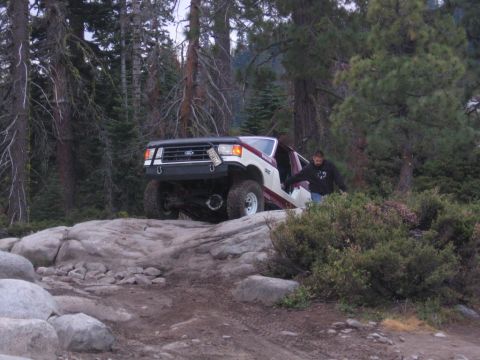 1989 Ford Bronco - A man exits a modified Ford Bronco as it navigates a rocky trail in a wooded area.
