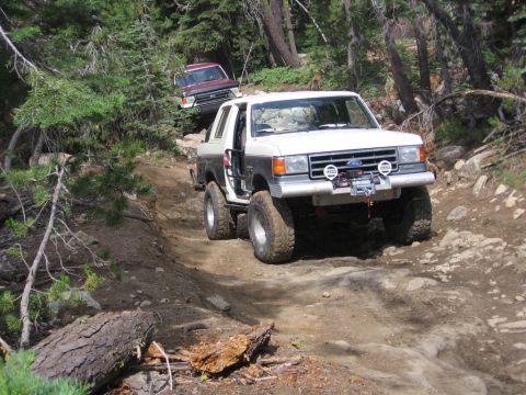 1989 Ford Bronco - A white and grey Ford Bronco navigates a challenging off-road trail with another vehicle behind it.