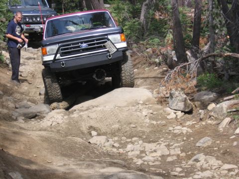 1989 Ford Bronco - This 1989 Ford Bronco is tackling a challenging off-road trail, with another vehicle visible in the background.