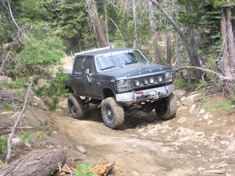 1989 Ford Bronco - This lifted 4x4 pickup truck navigates a rough, wooded trail with large off-road tires and a front-mounted winch.