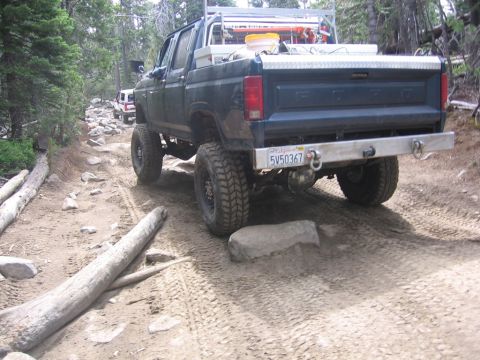 1989 Ford Bronco - A lifted pickup truck navigates a challenging, rocky off-road trail with another vehicle visible in the distance.