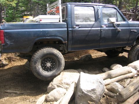 1989 Ford Bronco - This blue Ford F-Series truck is shown off-roading over rocks and logs.
