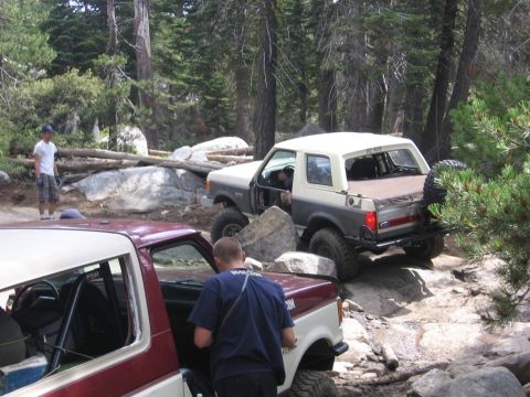 1989 Ford Bronco - Two off-road vehicles navigate a challenging rocky trail through a forest.