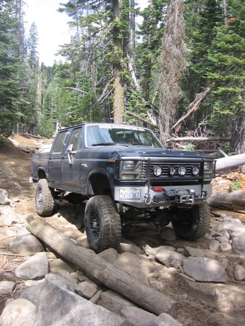 1989 Ford Bronco - Ford F-Series pickup truck navigating a challenging rocky trail in a forest.