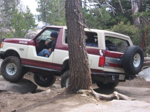 1989 Ford Bronco - A two-tone Ford Bronco navigates a rocky off-road course, with one wheel lifted.