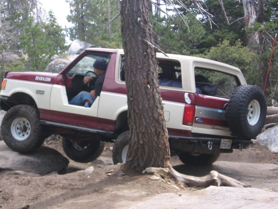 Ford Bronco climbing over rocks on a trail. Text on door says BOCKX.COM