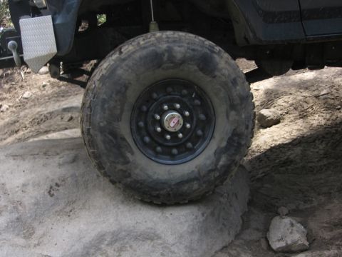 1989 Ford Bronco - The front wheel of a 1989 Ford Bronco is positioned on a rock, revealing its suspension and a diamond plate step.