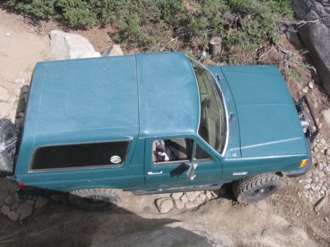 1989 Ford Bronco - A teal SUV navigates a challenging rocky terrain, its tires gripping the uneven ground.