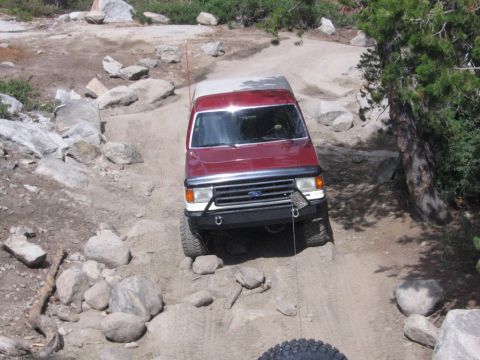 1989 Ford Bronco - 1989 Ford Bronco tackling an off-road trail with large rocks and trees.