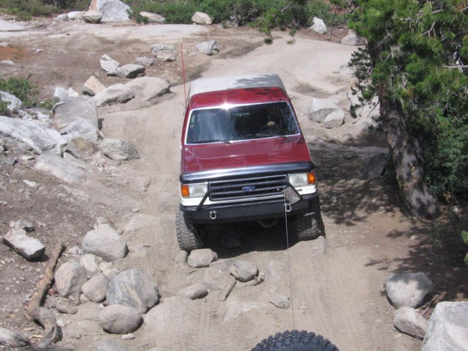 Red 1989 Ford Bronco navigating a rocky dirt trail, front view