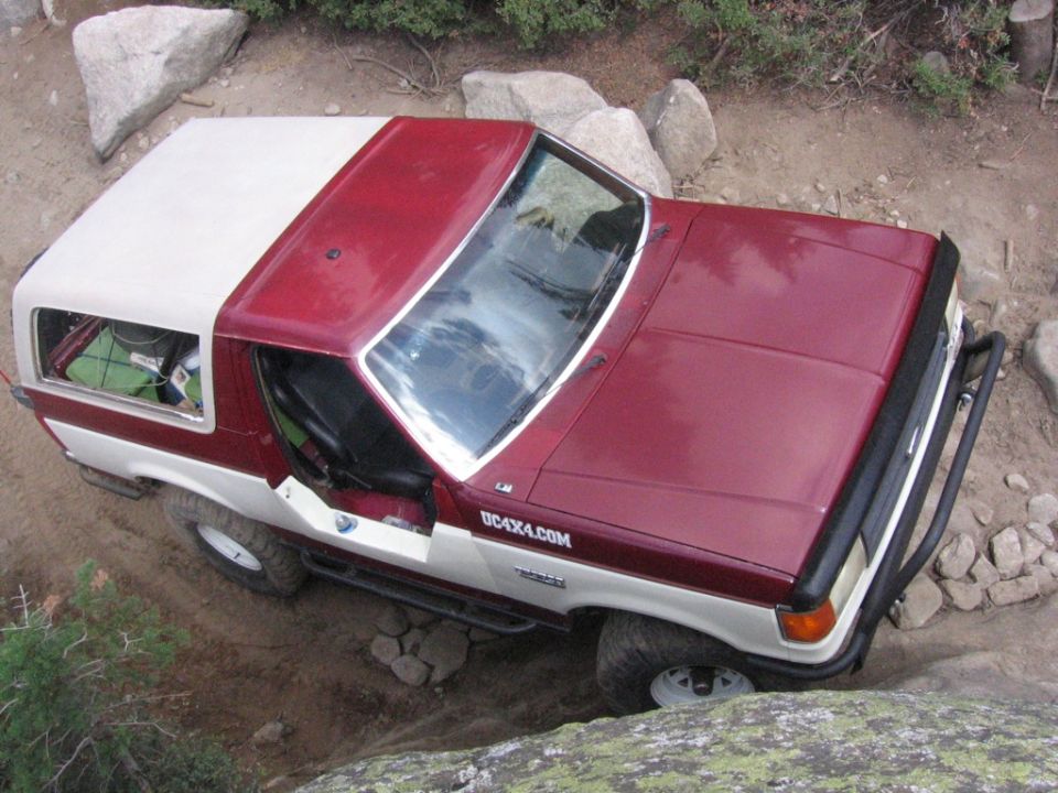 Two-tone red and white Ford Bronco off-roading over rocks. UC4X4.COM text on the side