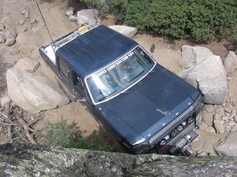 1989 Ford Bronco - This Ford Bronco is shown off-roading on a challenging, rocky path with dense foliage in the background.