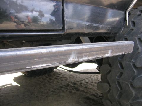 1989 Ford Bronco - Close-up view of the side of a black vehicle, showing the lower body panel, a metal step bar, and a large tire.
