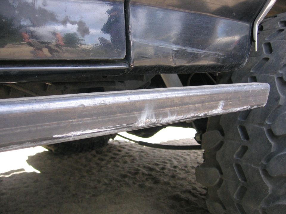 Side view of a black vehicle's lower body, step bar, and tire