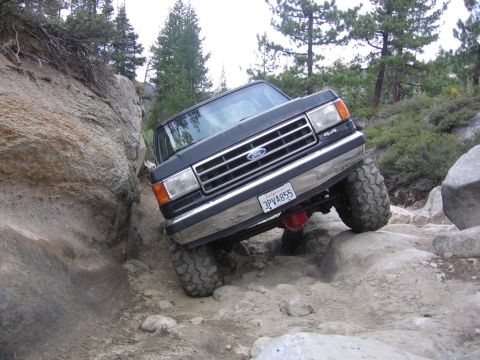 1989 Ford Bronco - Ford truck with lifted suspension and large tires crawling over rocks on an off-road trail.