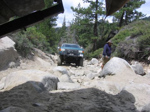 1989 Ford Bronco - 1989 Ford Bronco tackling a challenging off-road path through rocks and trees.