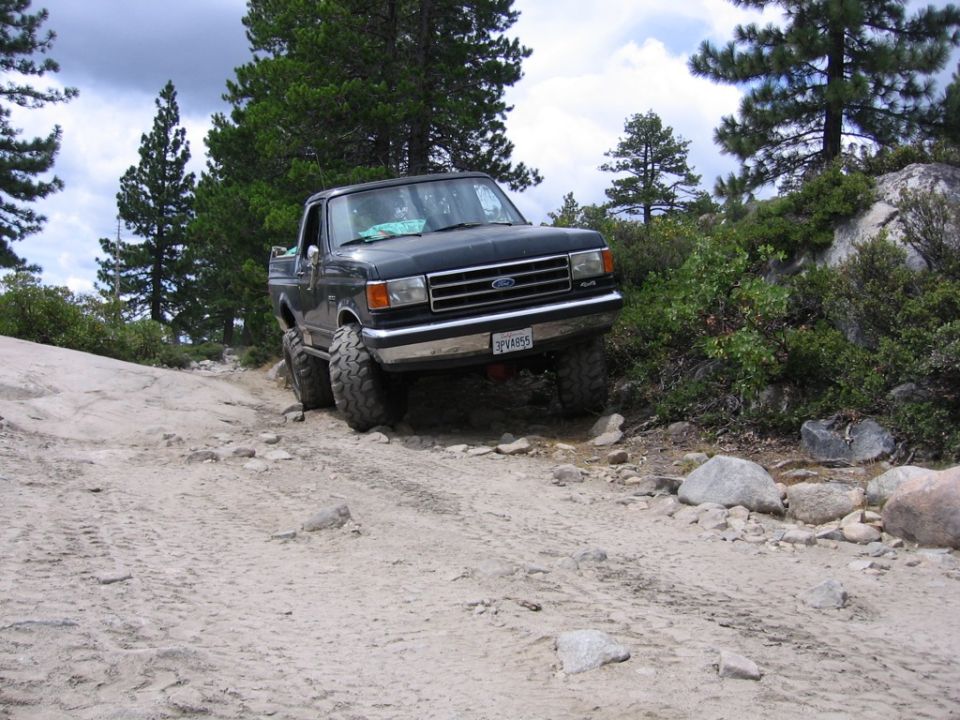 Dark blue 1987 Ford F-150 pickup truck with lifted suspension on a rocky, dirt road
