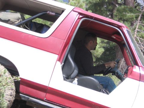 1989 Ford Bronco - A man is driving a red and white SUV with a roll cage visible inside.