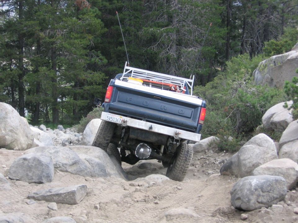 Dark blue Ford pickup truck navigating a rocky trail, rear view
