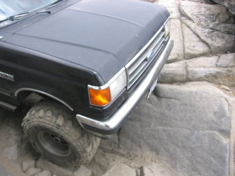 1989 Ford Bronco - This black Ford truck navigates a rocky terrain, its front end angled towards the viewer.