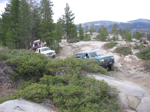 1989 Ford Bronco - Multiple 4x4 vehicles driving off-road on a rocky, wooded mountain trail.