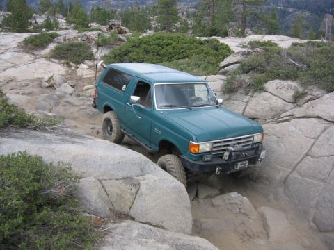 1989 Ford Bronco - A teal Ford Bronco tackles a challenging rocky terrain, demonstrating its off-road capabilities.