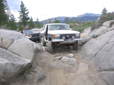 1989 Ford Bronco - Two off-road vehicles tackle a challenging rocky path in a mountainous area.