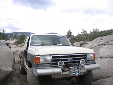 1989 Ford Bronco - A white and gray Ford Bronco navigates a rocky terrain with a winch mounted on the front bumper.