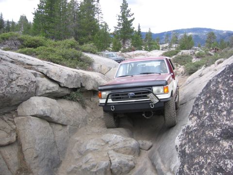 1989 Ford Bronco - 1989 Ford Bronco tackling a challenging off-road course on a sunny day.