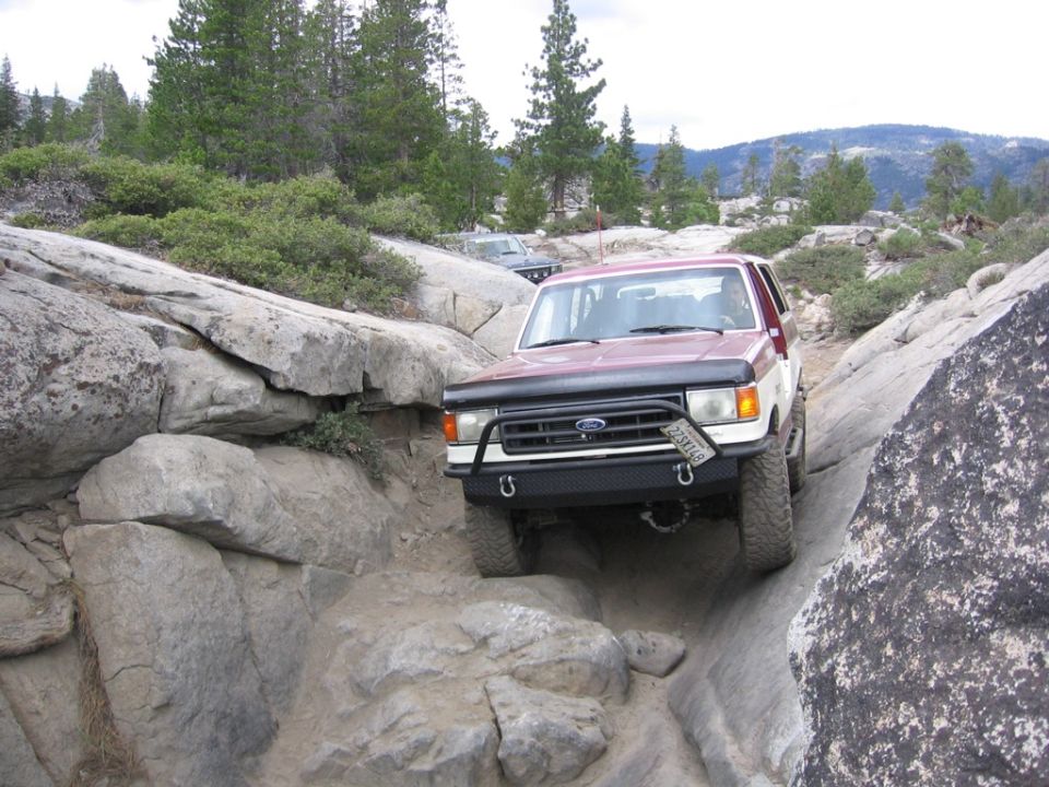 Maroon 1989 Ford Bronco navigating a narrow, rocky trail with another vehicle visible behind it