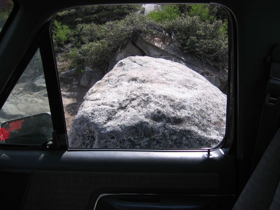 view from inside vehicle looking out window at large rock on a dirt path with bushes