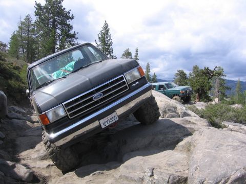 1989 Ford Bronco - A dark gray Ford Bronco navigates a rocky trail, with another green SUV visible in the background.