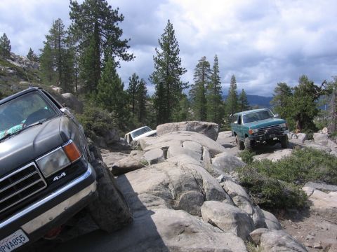 1989 Ford Bronco - Several off-road vehicles navigate a challenging rocky trail under a cloudy sky.