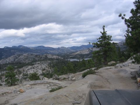 1989 Ford Bronco - A view from a vehicle's perspective shows a mountain landscape with a distant lake under a dramatic, cloudy sky.