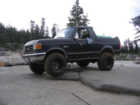 1989 Ford Bronco - This 1989 Ford Bronco is shown off-road on a rocky terrain with trees in the distance.
