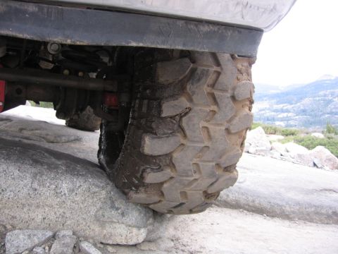 1989 Ford Bronco - A vehicle's tire is positioned on a large rock, with suspension parts visible.