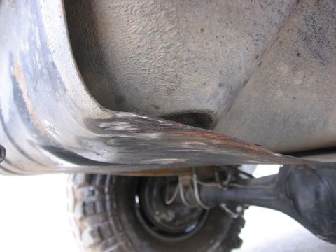 1989 Ford Bronco - Close-up view of the undercarriage of a vehicle, focusing on a damaged metal component and a tire.