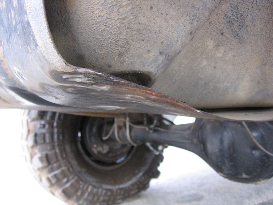 Undercarriage view of a vehicle's rear axle and tire, showing a dented metal component above