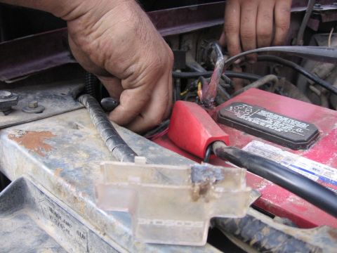 1989 Ford Bronco - Hands are seen working on the wiring and battery terminals in the engine bay of a vehicle.