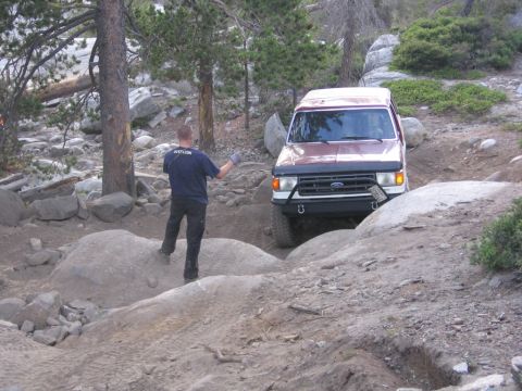 1989 Ford Bronco - A maroon Ford Bronco tackles a challenging off-road course, with a person observing the vehicle's progress.