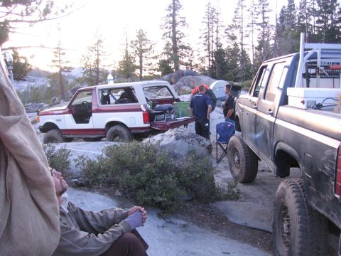 1989 Ford Bronco - A group of people and their off-road vehicles are gathered at a campsite in a wooded, rocky area.