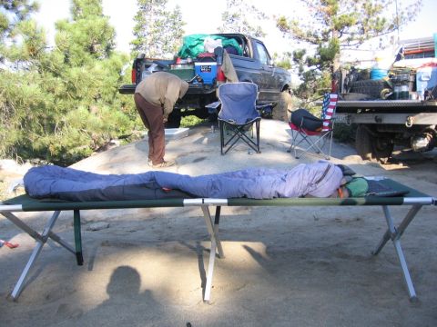 1989 Ford Bronco - Camping setup with cots and sleeping bags in front of pickup trucks.