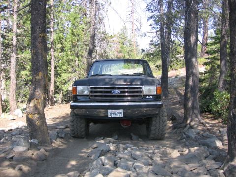 1989 Ford Bronco - 1989 Ford Bronco navigating a rough, rocky path through a forest.